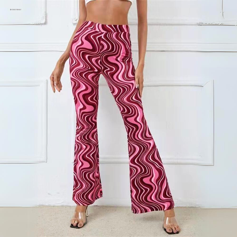 A woman stands against a white wall, wearing trendy statement pants in a pink and maroon swirled pattern and clear high-heeled sandals. Her midriff is bare, and her hands are relaxed at her sides.