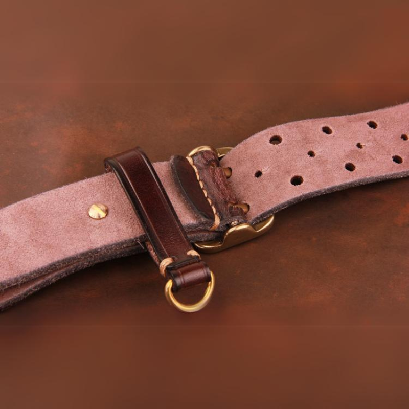 Close-up of a vintage leather belt with gold-colored metal buckle and ring, showing detailed stitching and multiple adjustment holes on a rustic brown background.