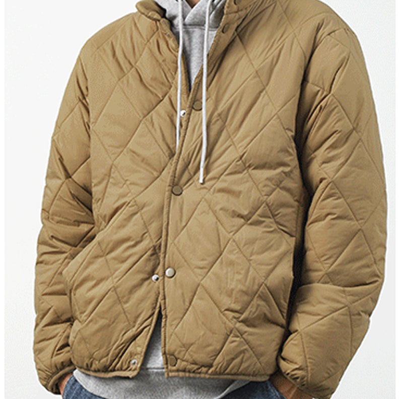 A person wearing a tan, diamond-stitched padded jacket over a gray hoodie with white drawstrings, standing against a plain light background.