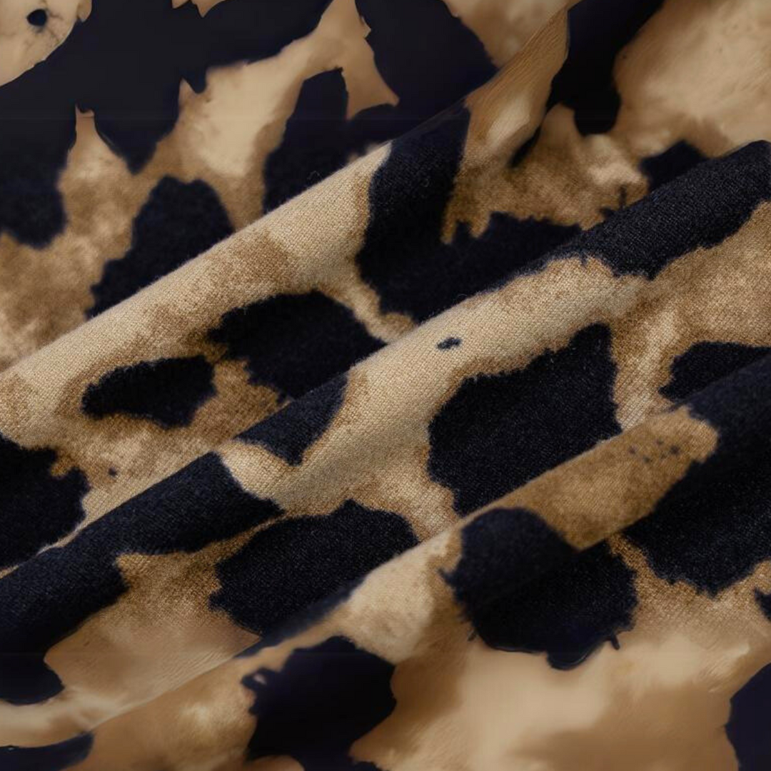Close-up of fabric from a leopard print dress, featuring brown and black irregular spots on a beige background. The soft texture and bold pattern make it perfect for a summer statement dress.