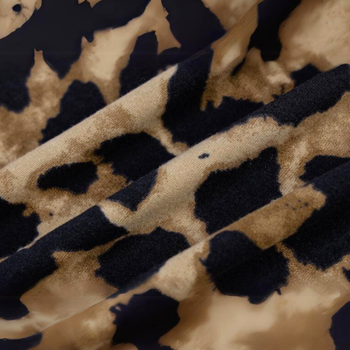Close-up of fabric from a leopard print dress, featuring brown and black irregular spots on a beige background. The soft texture and bold pattern make it perfect for a summer statement dress.