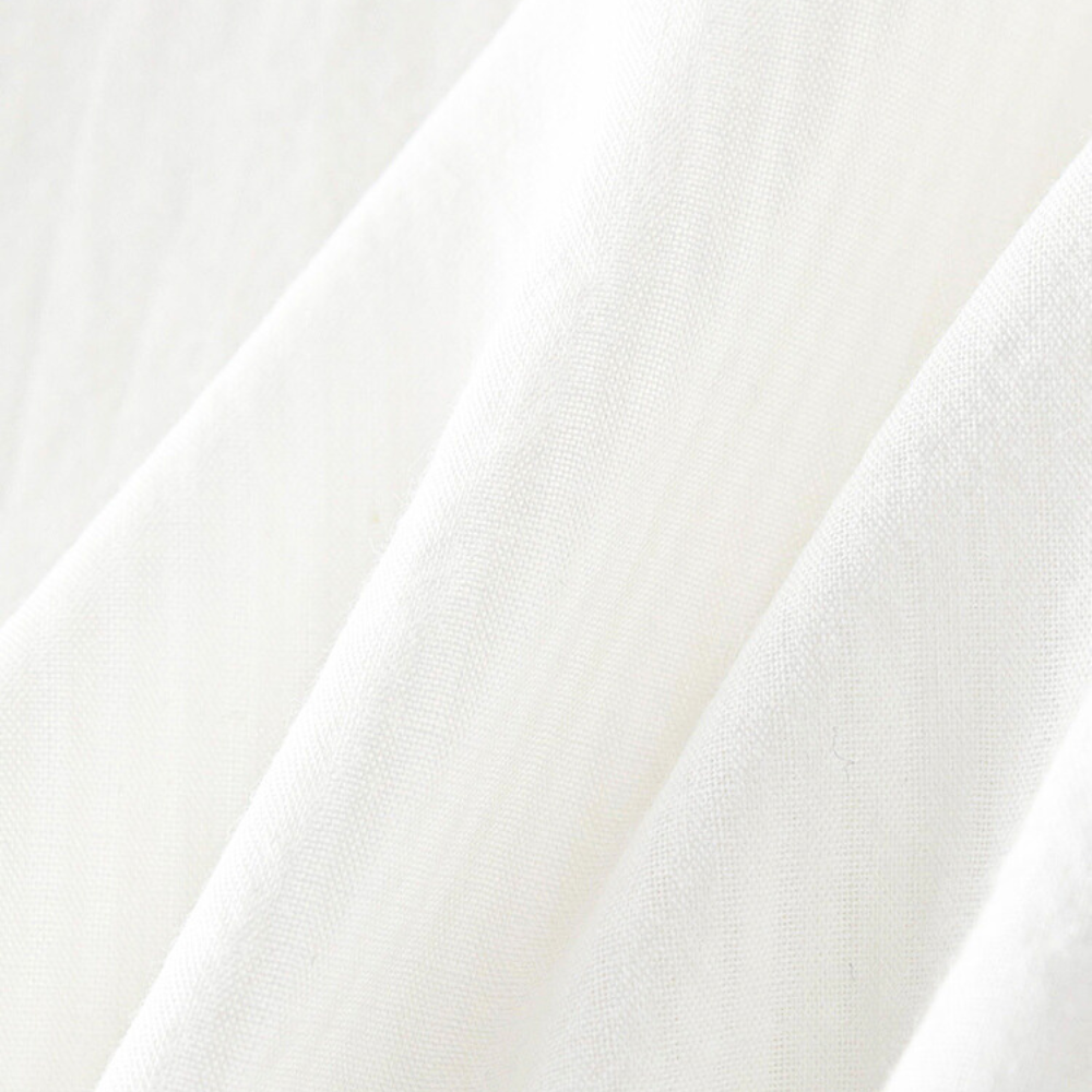 Close-up of soft, white fabric with gentle folds and a slightly textured surface, highlighting the smooth and delicate appearance of this versatile blouse.