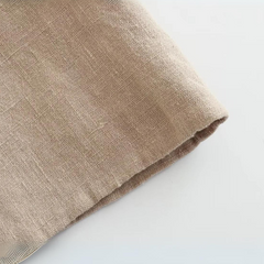 A close-up of a beige linen fabric laid on a white surface, showing its textured weave and unfinished edge—perfect for crafting summer style essentials like wide-leg pants.
