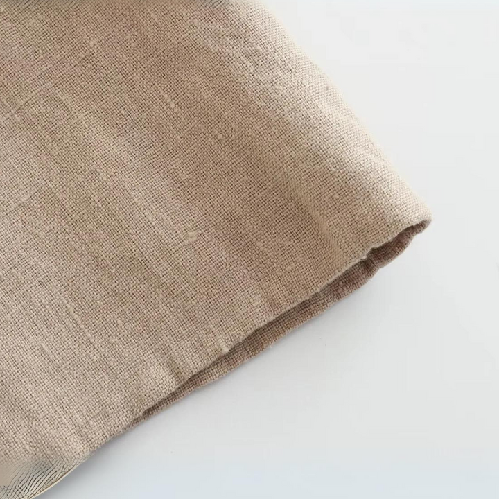 A close-up of a beige linen fabric laid on a white surface, showing its textured weave and unfinished edge—perfect for crafting summer style essentials like wide-leg pants.