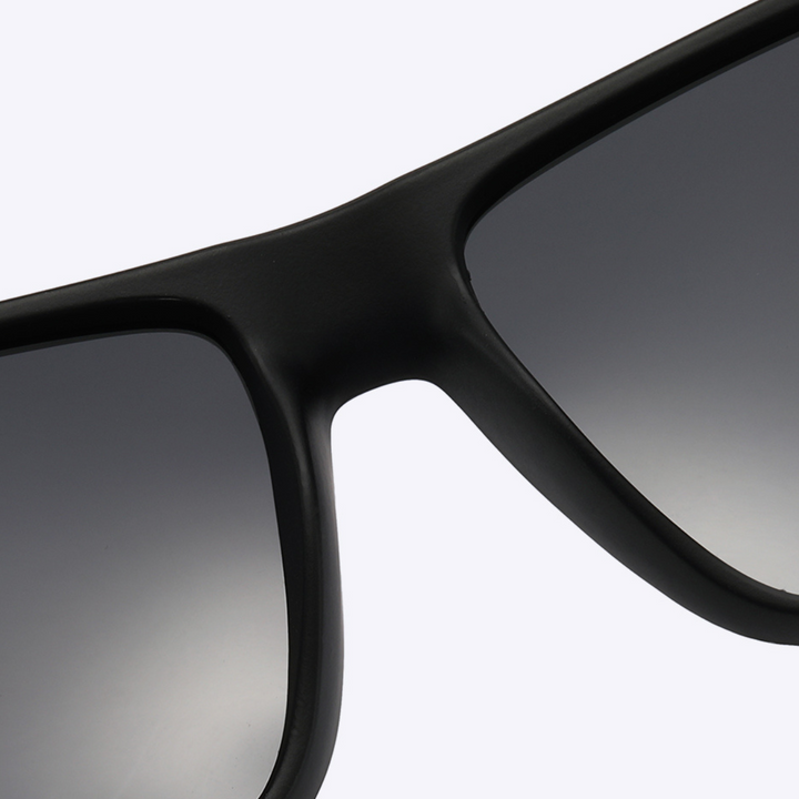 Close-up view of the top part of stylish sunglasses with black frames and dark, gradient-tinted lenses, set against a light background.