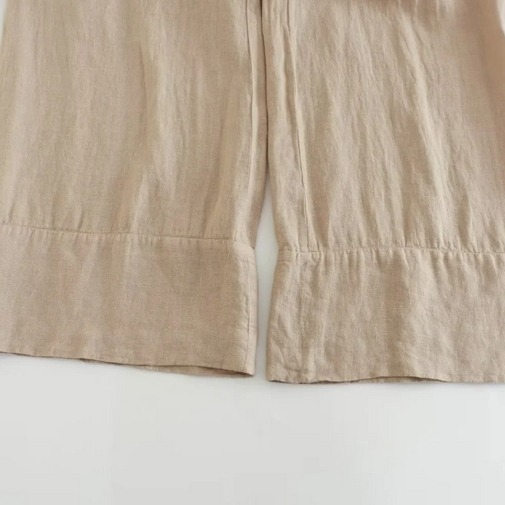 Close-up of the bottom hem of beige wide-leg pants laid flat on a white surface, showing straight, clean stitching and slightly wrinkled fabric texture—perfect for effortless summer style.