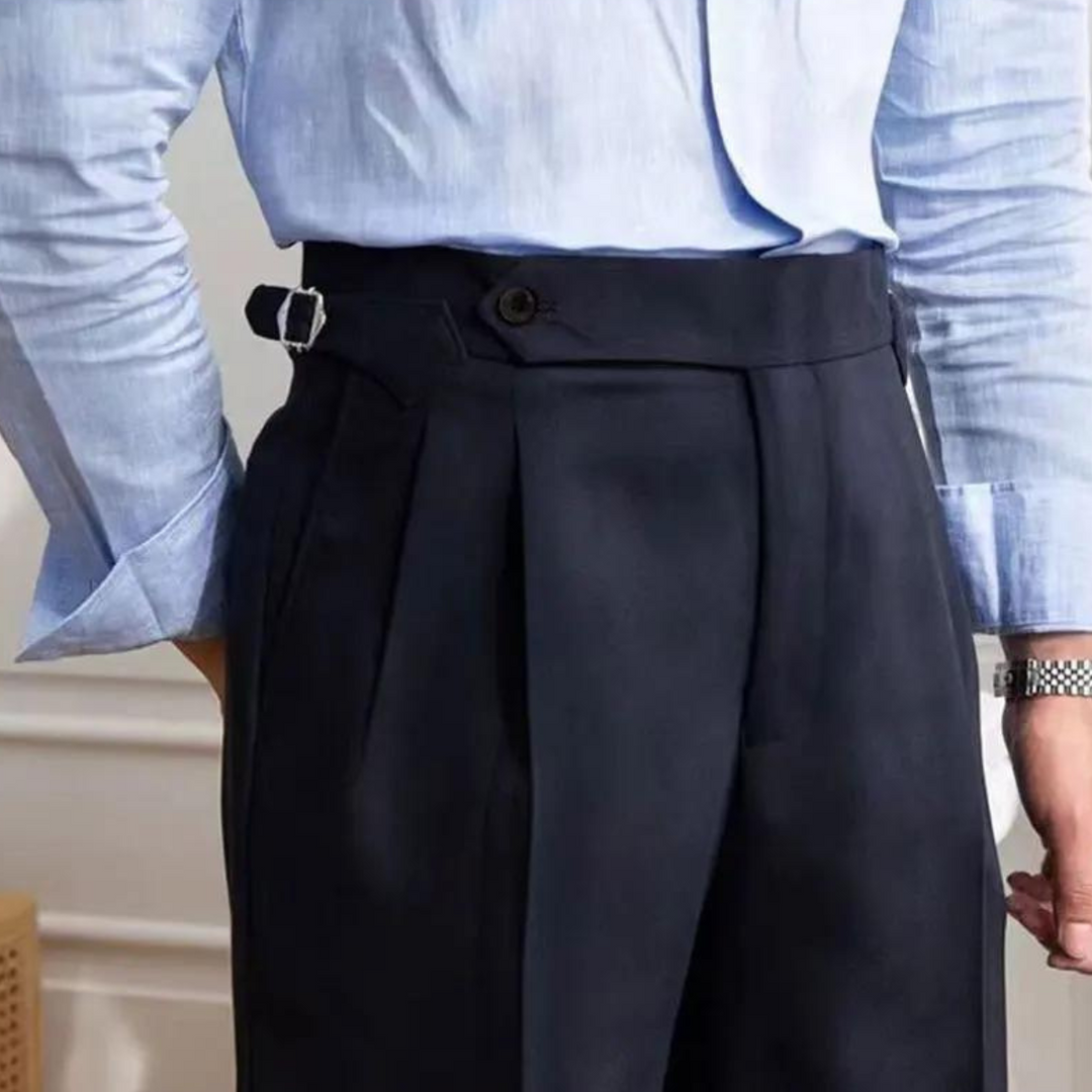 A person embodying the old money aesthetic wears a light blue dress shirt tucked into high-waisted, pleated navy trousers with side adjusters. The tailored fit highlights sophistication, while a wristwatch peeks from the left arm.