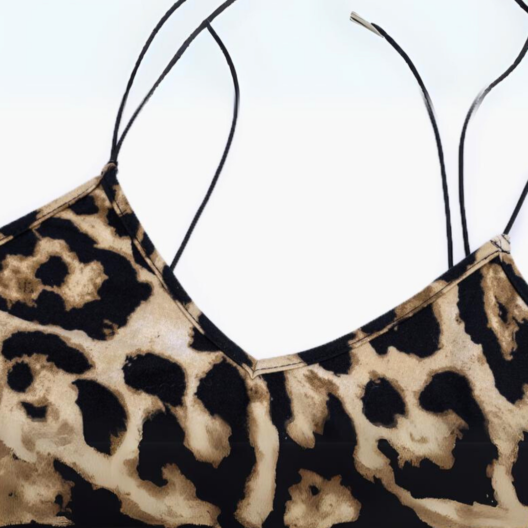 A close-up of a leopard print dress with thin black spaghetti straps against a white background, perfect for making a bold summer statement.