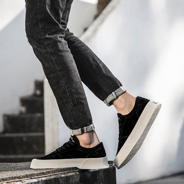 A person wearing rolled-up black jeans and stylish lace-up sneakers with thick white soles, designed for comfortable cushioning, is shown standing on outdoor stone steps, with one foot raised as if in motion.