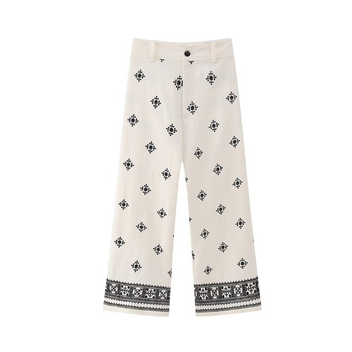 White wide-leg trousers with black geometric and floral embroidery scattered throughout and a decorative embroidered border near the hem. These boho chic pants feature a button and zip closure for easy wear.
