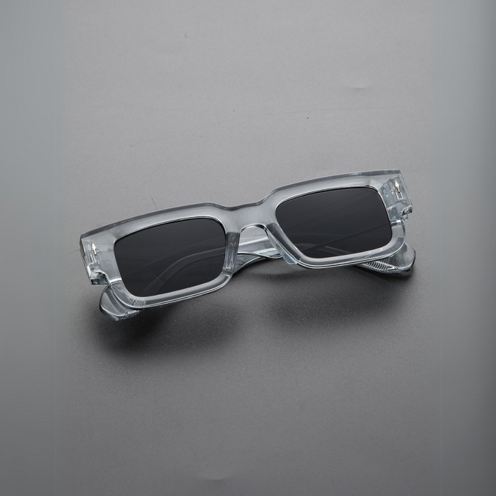 Clear rectangular sunglasses with UV400 protection rest on a flat gray surface. The lightweight sunglasses feature transparent, bold angular frames and black-tinted lenses for a modern, stylish look.