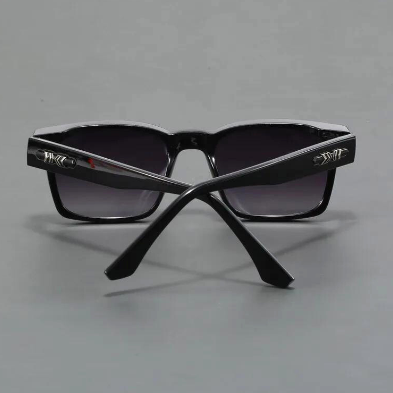 A pair of black sunglasses with dark lenses, shown from the back with the arms crossed. The durable frames feature metallic decorative details near the hinges. The background is a plain gray surface.