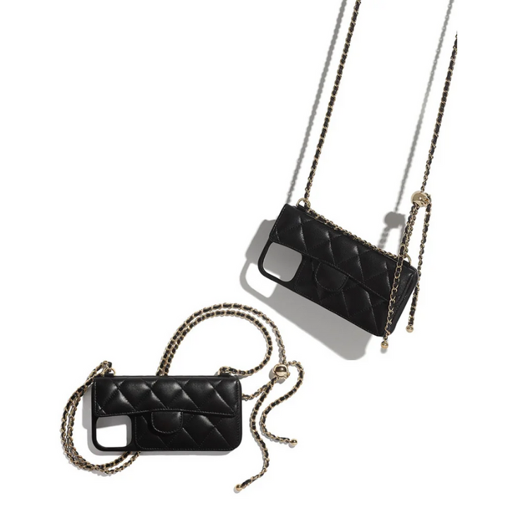 Two black quilted phone cases with stylish chain straps are laid out on a white surface, casting shadows. The chains are intertwined, and each case has a camera cutout and a small pocket on the front.