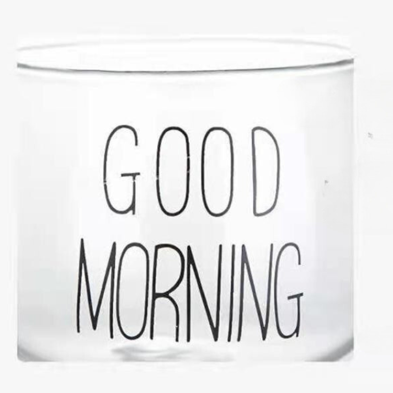 A transparent glass cup with a clear design and the words GOOD MORNING printed in bold, black letters on its side.
