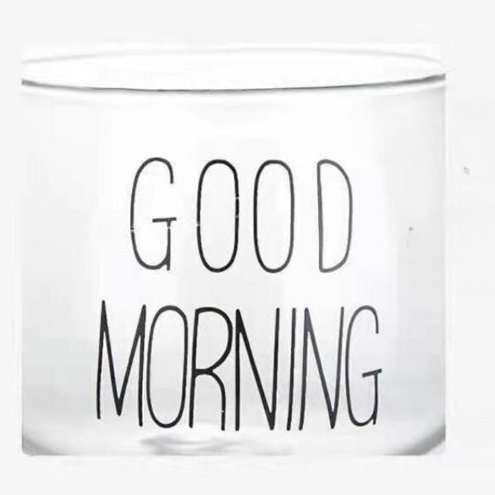 A transparent glass cup with a clear design and the words GOOD MORNING printed in bold, black letters on its side.