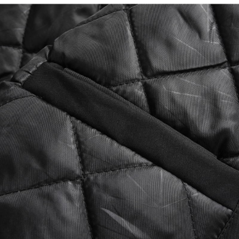Close-up of black quilted fabric with diagonal stitching and a smooth black band crossing the center, showcasing the slightly shiny texture and geometric pattern of this windproof jacket.