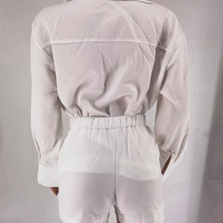 Person wearing a white long-sleeve linen set and high-waisted pants, photographed from the back against a plain light background. The sustainable linen fabric appears slightly sheer.