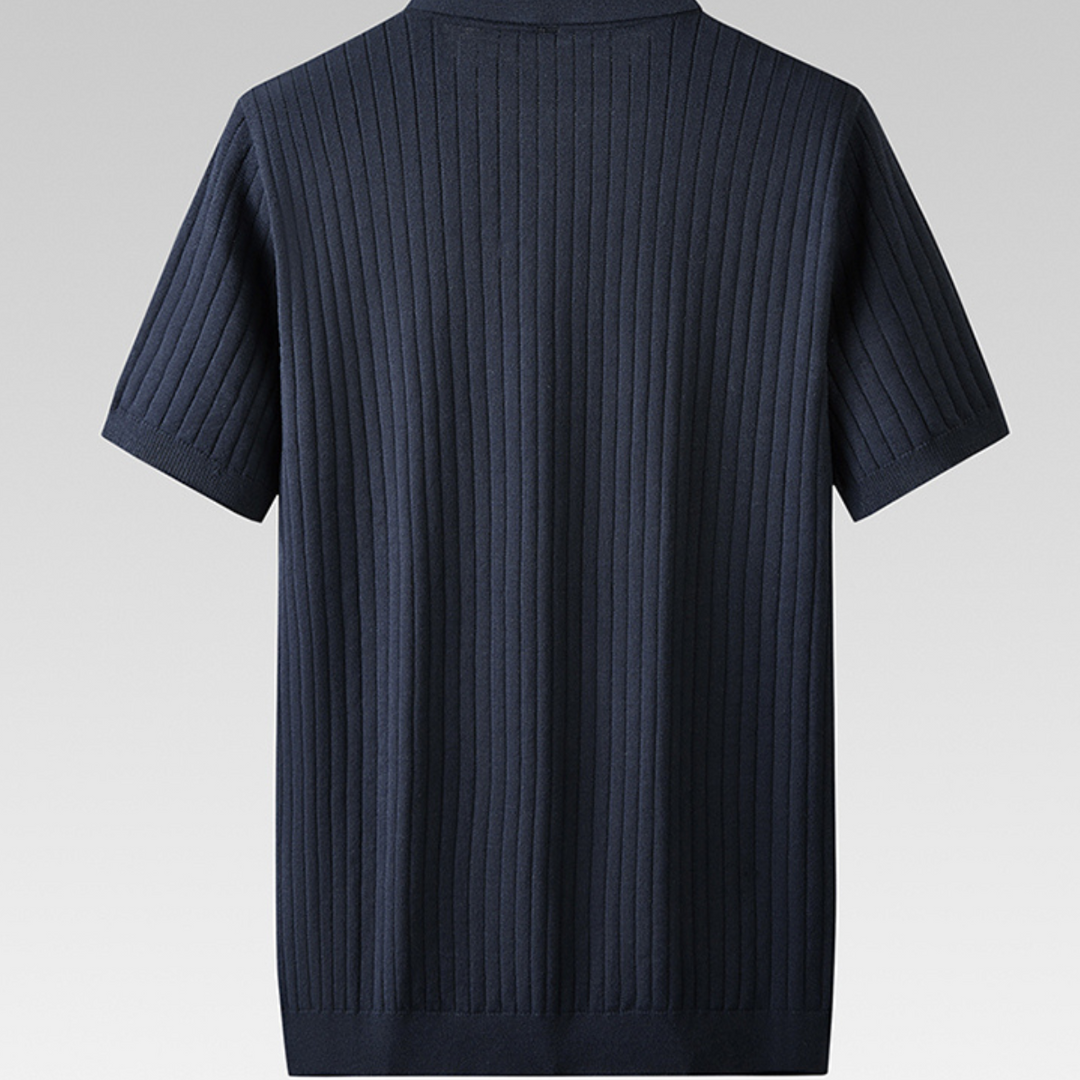 A short-sleeved, dark blue ribbed knit polo is shown from the back against a plain light gray background. The shirt features vertical ribbed detailing and a simple, collarless neckline for an urban professional look.