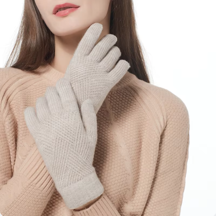 A woman wearing a textured beige cashmere blend sweater and light gray knit gloves stands against a white background with her gloved hands crossed in front of her chest. Her face is partially visible.