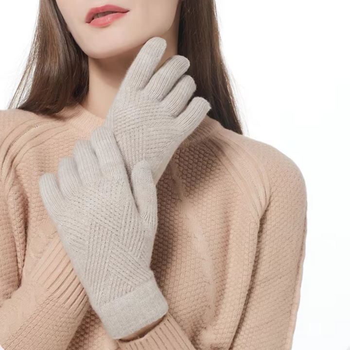 A woman wearing a textured beige cashmere blend sweater and light gray knit gloves stands against a white background with her gloved hands crossed in front of her chest. Her face is partially visible.