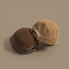 Two Japanese-style peaked caps in brown and tan are placed side by side on a plain beige background, both displaying the adjustable strap with metal buckles at the back.