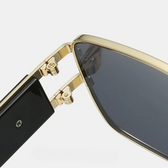 Close-up view of the hinge connecting the gold and black arm of these bold sunglasses to the dark-tinted lens frame, showing the detailed metal hardware found in premium metal frames.