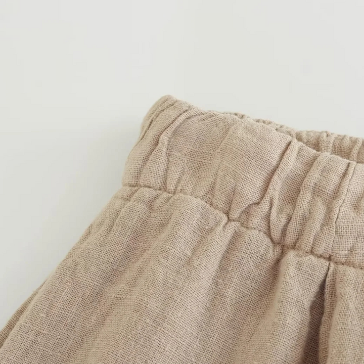 Close-up of the waistband of beige linen wide-leg pants, featuring gathered fabric and an elastic waistband, set against a plain light background—perfect for effortless summer style.