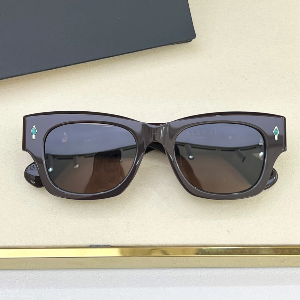 A pair of vintage-inspired rectangular dark brown sunglasses with UV400 protection and dark lenses, featuring small turquoise diamond-shaped accents on the upper corners of the frame, resting on a beige surface.