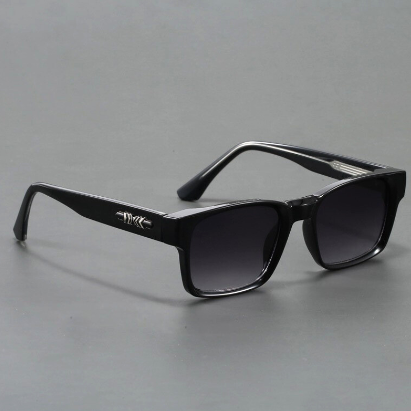 A pair of black rectangular sunglasses with modern design, featuring dark lenses and a silver decorative detail on the arms, displayed on a plain gray surface.