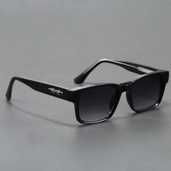 A pair of black rectangular sunglasses with modern design, featuring dark lenses and a silver decorative detail on the arms, displayed on a plain gray surface.