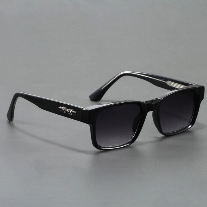 A pair of black rectangular sunglasses with modern design, featuring dark lenses and a silver decorative detail on the arms, displayed on a plain gray surface.