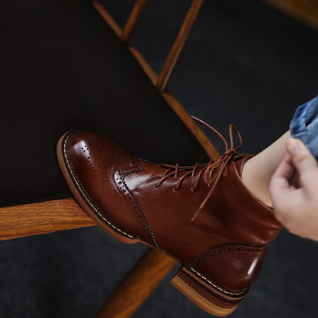 A person’s hand tying a brown genuine leather shoe.