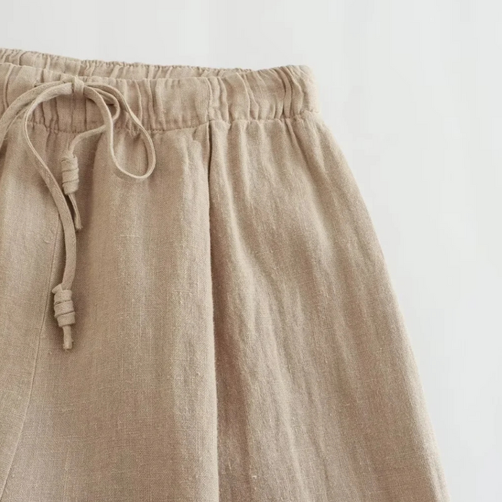 Close-up of beige linen wide-leg pants with an elastic waistband and drawstring ties, shown against a plain white background—perfect for effortless summer style.