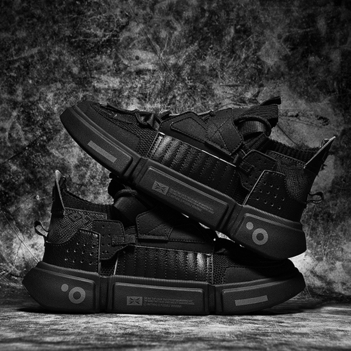 A pair of black Extreme VS7 Sneakers are stacked on top of each other against a textured, grunge-style background. These streetwear sneakers feature thick soles, mesh panels, and geometric accents for a bold, futuristic look.