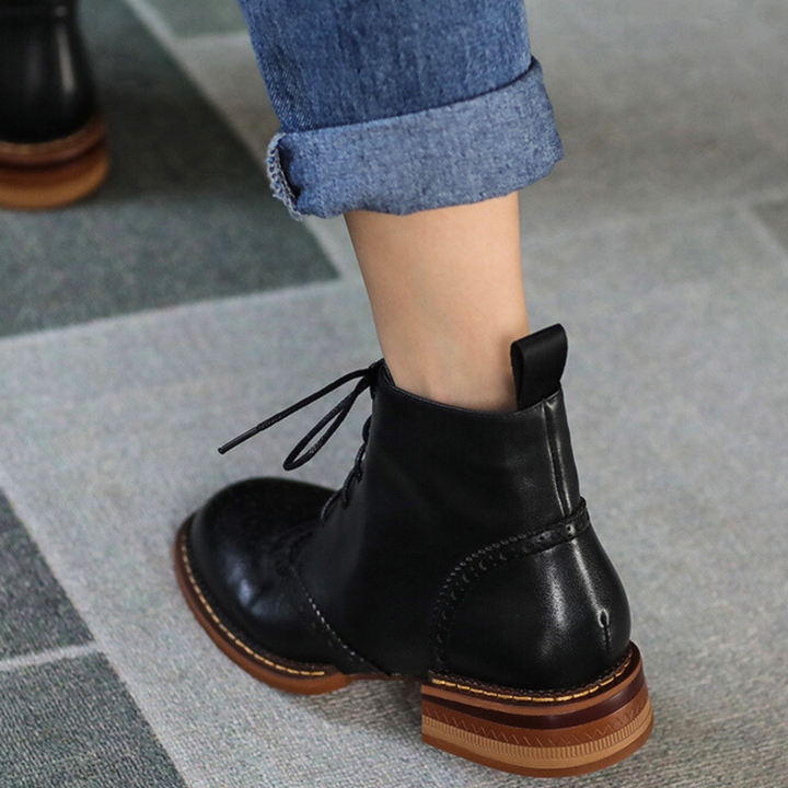 A true urban trendsetter, wearing rolled-up blue jeans and genuine leather lace-up ankle boots with brown soles, walks on a tiled floor.