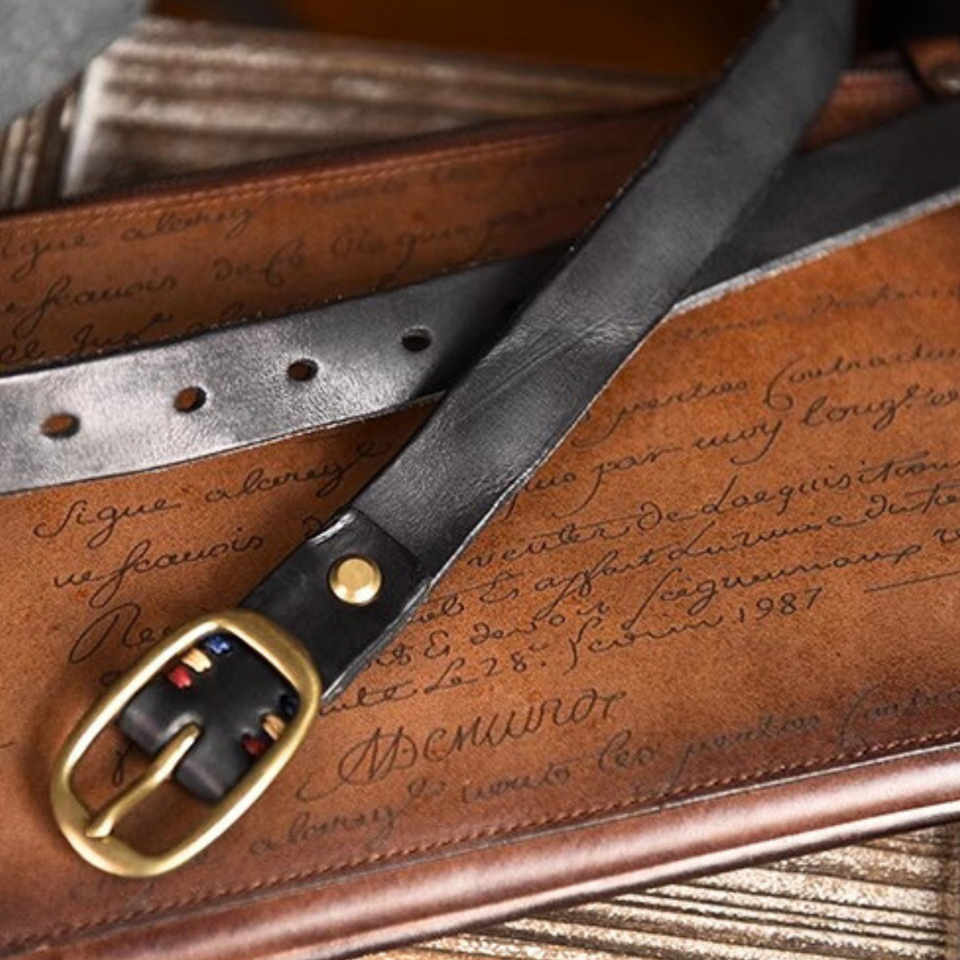 A classic black leather belt with a gold buckle rests on a brown leather surface embossed with cursive writing, capturing the timeless elegance of country fashion favored by Southern ladies.