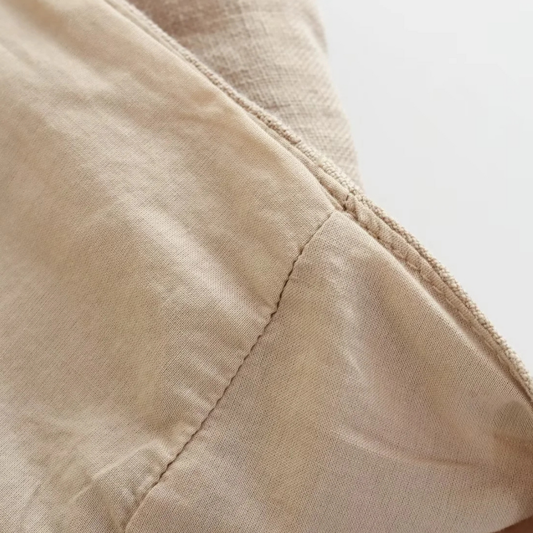 Close-up of light beige fabric with a visible seam, showing the texture and stitching detail. Perfect for wide-leg pants, the material appears soft and slightly wrinkled, with natural lighting highlighting its surface.