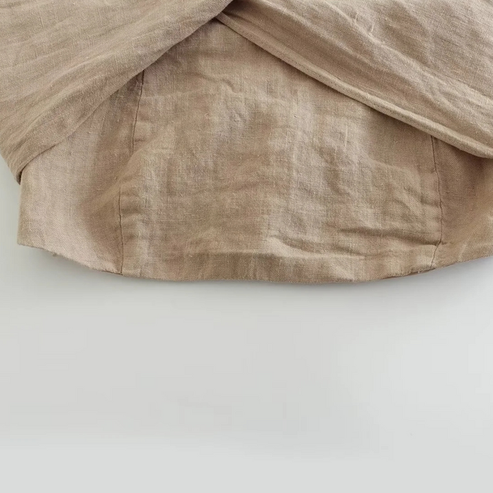 A close-up of a beige linen fabric with visible texture and stitching, draped in soft folds over a light surface—perfect for summer style essentials like chic halter collars or breezy wide-leg pants.