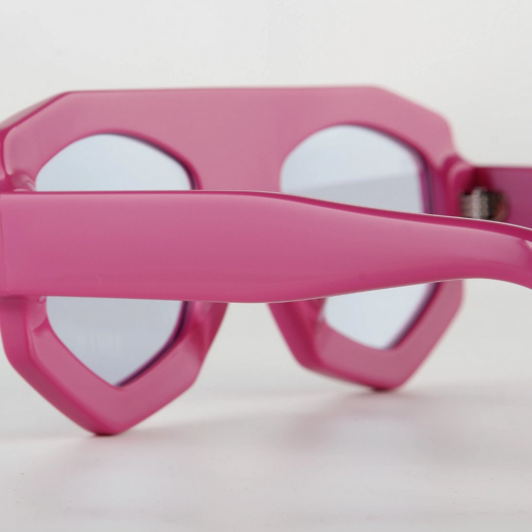 Close-up of pink geometric sunglasses with thick acetate frames and mirrored lenses, offering UV400 protection, photographed against a plain white background.