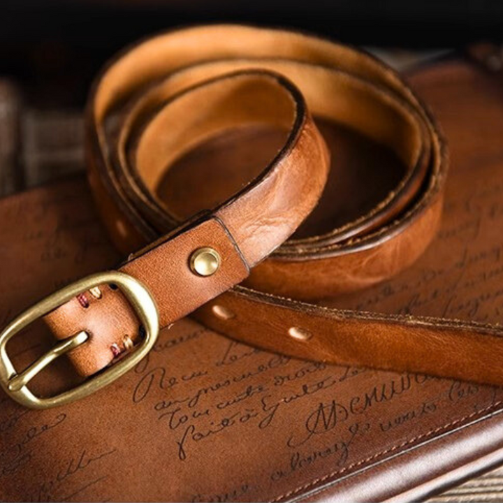 A coiled brown leather belt with a brass buckle rests on a brown surface with cursive writing, its texture and stitching details clearly visible—a perfect touch for country fashion beloved by Southern ladies.