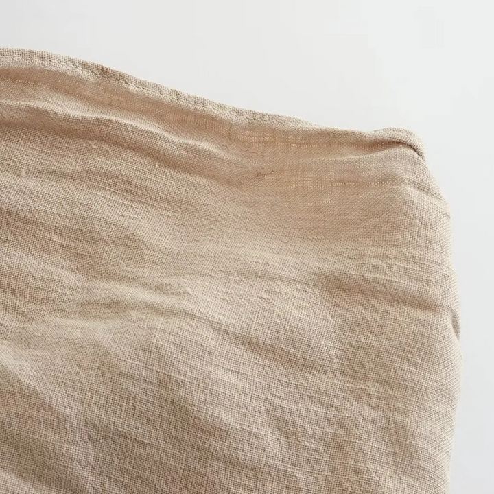 A close-up view of a piece of light beige, textured fabric with visible weaves, slightly wrinkled and spread out against a plain white background—perfect for crafting chic halter collar tops or wide-leg pants in an effortless summer style.
