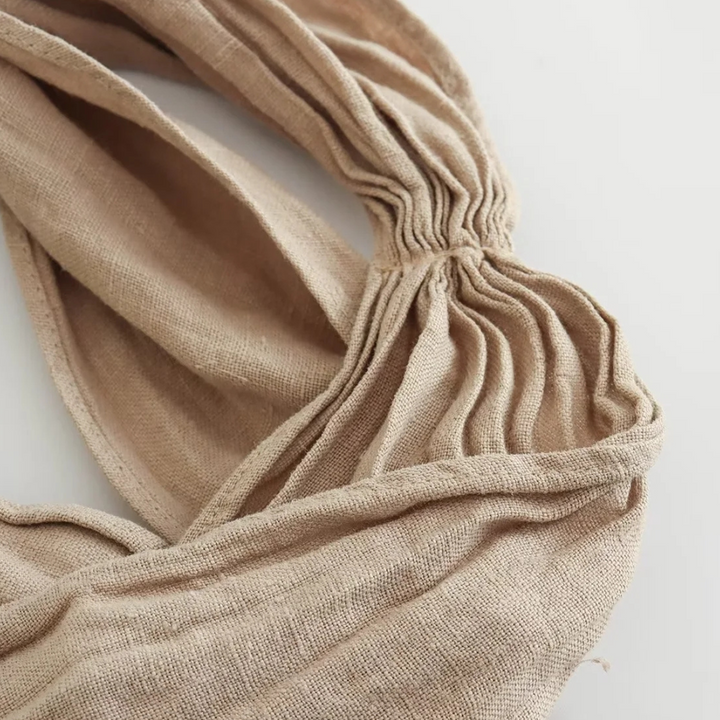 A close-up of a beige, textured fabric with gathered pleats and soft folds, arranged in overlapping layers on a white background—perfect for elevating summer style or adding interest to chic halter collar wide-leg pants.