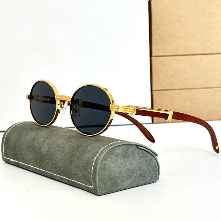Vintage round sunglasses with gold frames and dark lenses rest on a gray, velvet-like case. Featuring wooden temples that are slightly curved, these shades offer both style and UV400 protection. A stack of tan boxes decorates the white background.