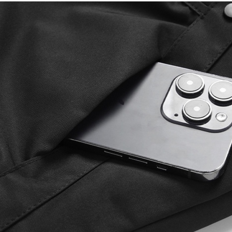 A silver smartphone with three camera lenses peeks out from the pocket of black pants, next to a windproof jacket with adjustable cuffs.