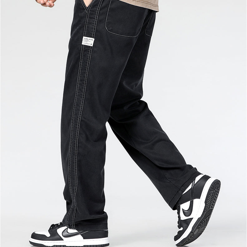 A person wearing Summer Loose Men Jeans with white stitching and black-and-white Nike sneakers walks on a light background. The upper body is partially visible, and a small label is seen on these wide-leg denim trousers.