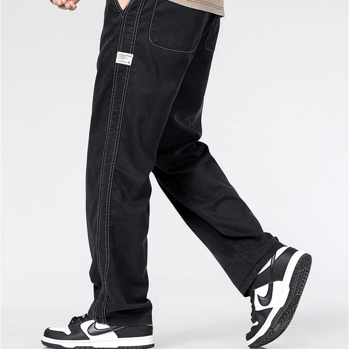 A person wearing Summer Loose Men Jeans with white stitching and black-and-white Nike sneakers walks on a light background. The upper body is partially visible, and a small label is seen on these wide-leg denim trousers.