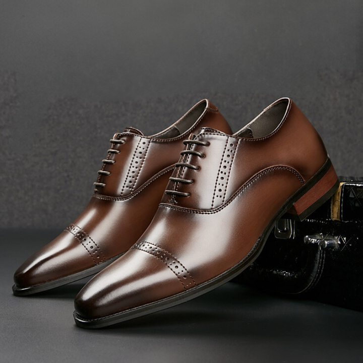 A pair of polished brown Italian leather dress shoes with laces and decorative broguing, displayed against a dark background. The classic, formal design features a slight sheen, cap toe detailing, and elegant hand-stitched detailing.