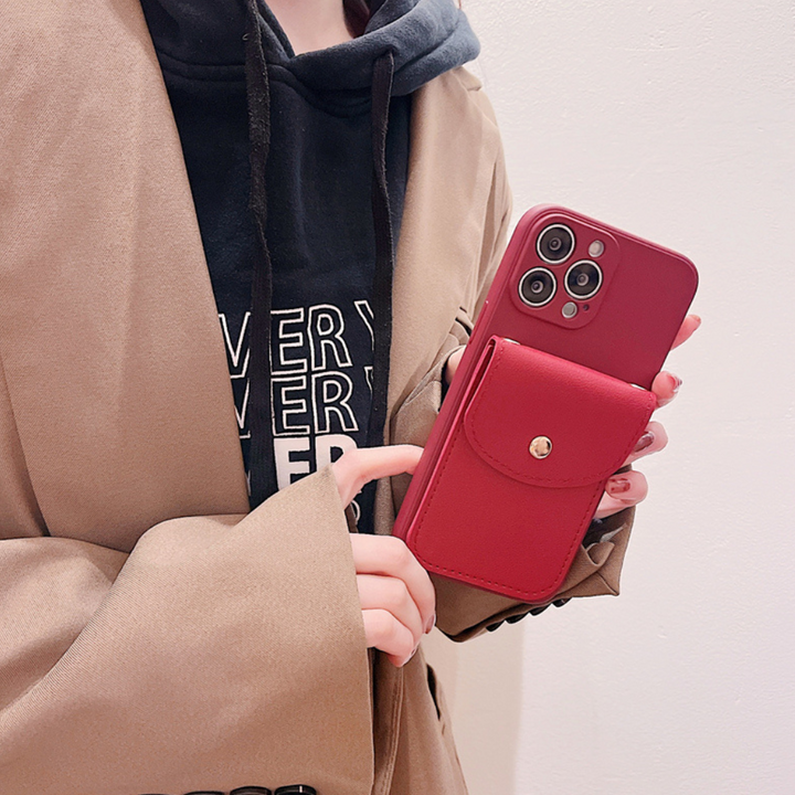 A person in a tan coat and black hoodie holds a red smartphone with a matching phone case wallet featuring a secure cardholder on the back. The phone, with three camera lenses, is set against a plain white background.