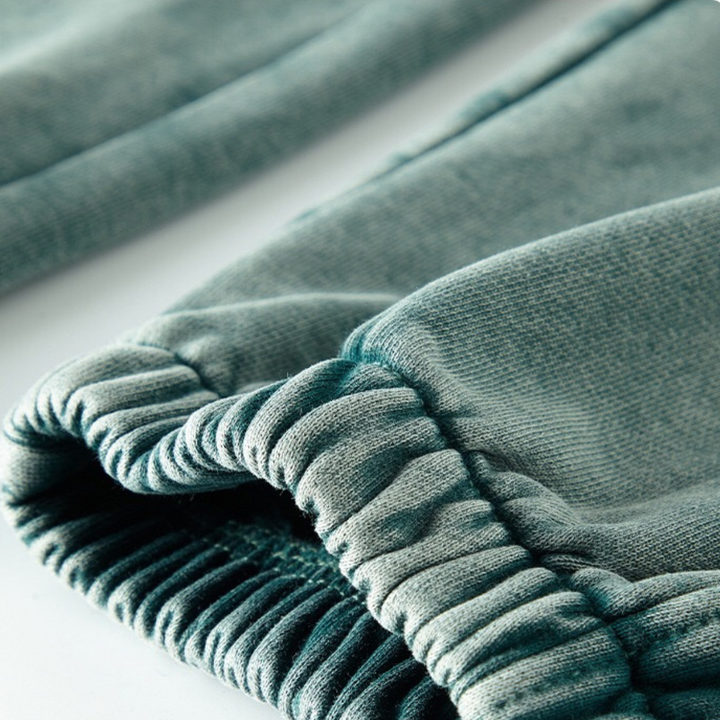 Close-up of the tapered cuffs and elastic waistband on a light teal or greenish-blue velvet or fleece garment, possibly sweatpants or a sweatshirt, shown on a white background.