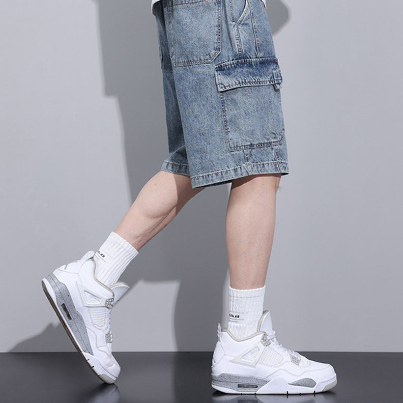 A person wears light blue men’s denim shorts with an elastic waist, paired with white crew socks and white sneakers, standing in side profile against a plain gray background, shown from the waist down.